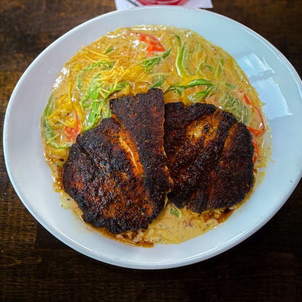 Blackened fish fillets served with creamy pasta, green peppers, and red peppers in a white bowl.