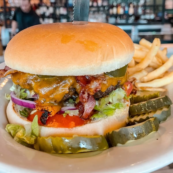 A large bacon cheeseburger with lettuce, tomato, onion, and pickles, served with fries.