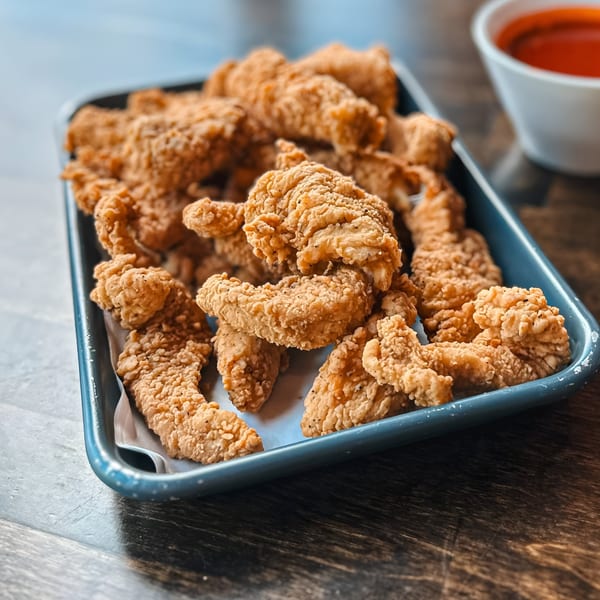 Crispy fried shrimp or chicken tenders in a blue tray with a side of red dipping sauce.