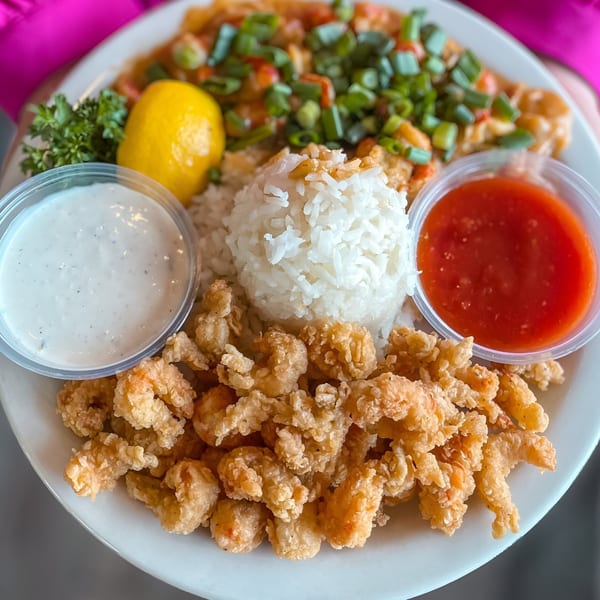 A plate of fried shrimp, rice, shrimp etouffee, lemon, parsley, ranch, and sweet chili sauce.