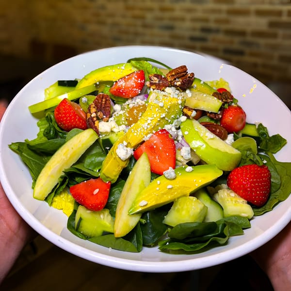 A vibrant salad with spinach, strawberries, avocado, pecans, and crumbled cheese in a white bowl.